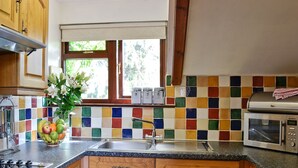 Een keuken met houten kastjes, een granieten aanrecht, een roestvrijstalen spoelbak, een magnetron en een raam met uitzicht op groen.