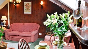 Een gezellige eethoek met een houten tafel gedekt voor twee personen, een roze bank en een vaas witte bloemen.