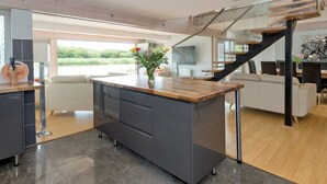 Una cocina moderna con una isla central, un comedor con una escalera de cristal y vistas al exterior.