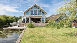 Una casa moderna con una terraza grande, un muelle privado y un césped.