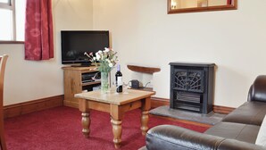 Ein Wohnzimmer mit Fernseher, Kamin, Holztisch mit Blumenvase und Ledersofa.