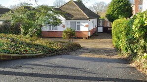 A residential property with a gravel driveway, a small garden, and a house with a tiled roof and brickwork.