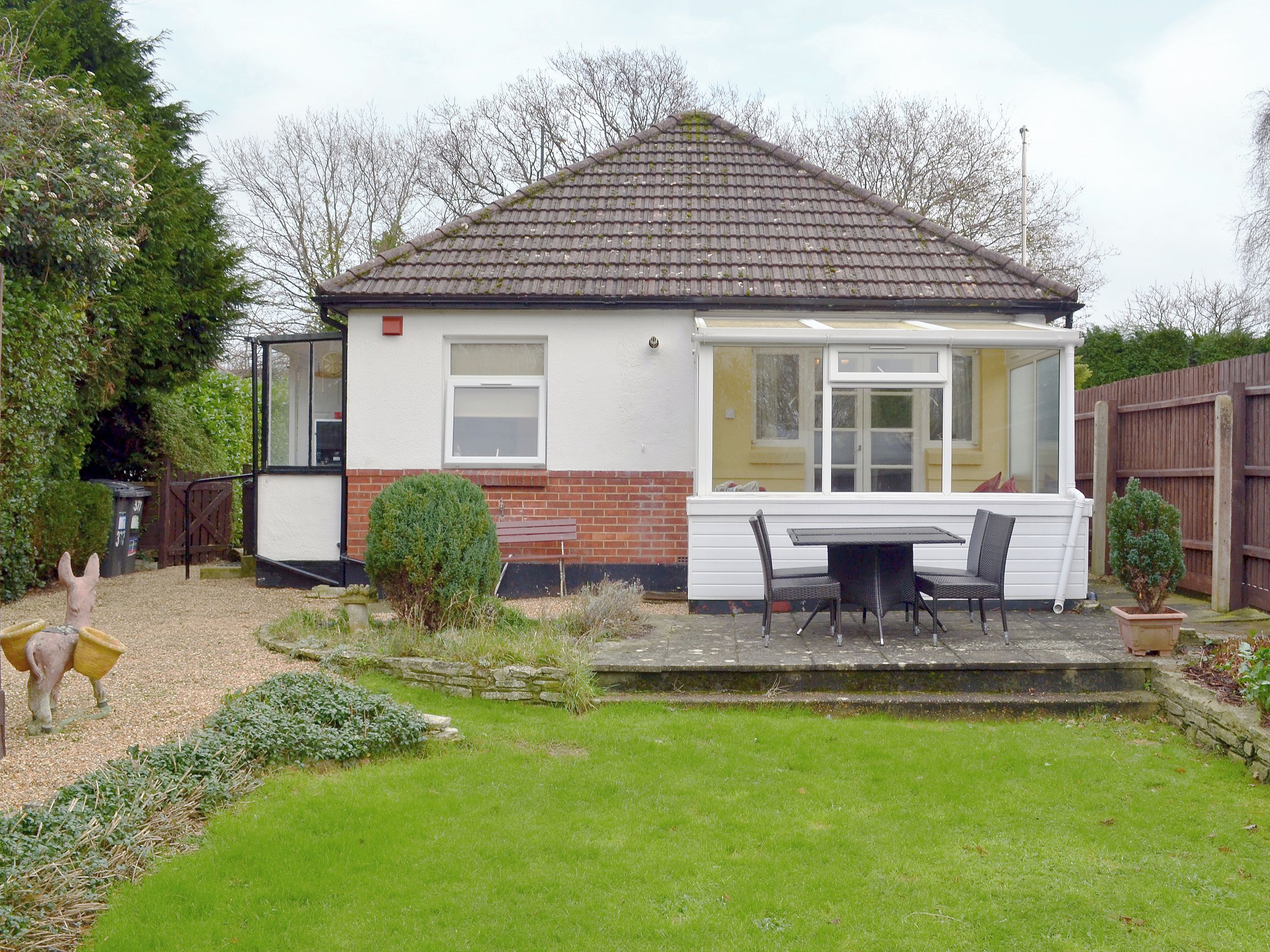 A house with a conservatory, a patio with a table and chairs, and a small garden with a statue.