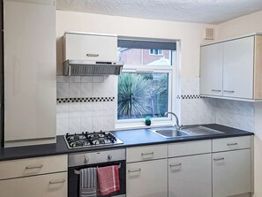 A modern kitchen with white cabinets, a gas stove, a sink, and a window with a view of greenery. - 2 bedroom accommodation in Bournemouth (Bournemouth)
