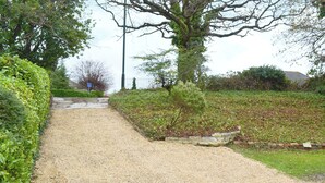 A gravel path flanked by green hedges and a stone wall, leading to a building with a tiled roof.