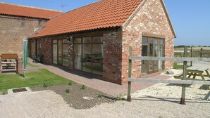 A brick building with a red-tiled roof, large glass windows, and a wooden fence. - Kingfisher Cottage - 25114 (Flamborough)