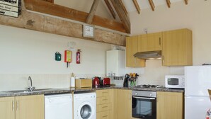A kitchen with wooden cabinets, a washing machine, a stove, and a microwave. - Kingfisher Cottage - 25114 (Flamborough)