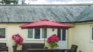 An outdoor seating area with a table and chairs, a red umbrella, and potted plants.