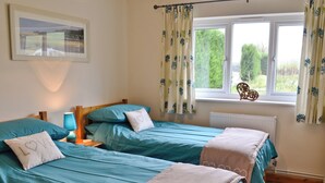 A bedroom with two single beds, a nightstand with a lamp, a window with curtains, and a radiator.