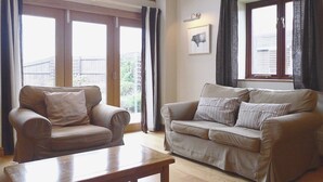 Ein Wohnzimmer mit einem braunen Ledersofa, einem Holztisch und großen Fenstern mit Vorhängen.