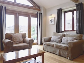Ein Wohnzimmer mit einem braunen Ledersofa, einem Holztisch und großen Fenstern mit Vorhängen.