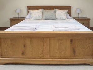 Una cama bien hecha con cabecera de madera, dos mesitas de noche con lámparas y suelo cubierto de alfombra.
