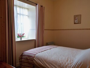 A bedroom with a bed, a window with curtains, a radiator, and a small picture on the wall.