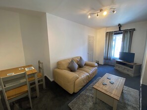 A living room with a sofa, a TV on a stand, a wooden table, a chair, and a door.