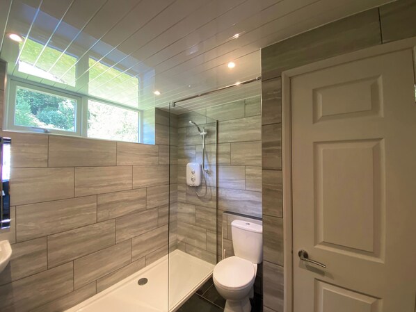 Une salle de bain équipée d’une douche, de toilettes et d’un lavabo, avec un design moderne caractérisé par des carreaux gris et une cloison en verre.