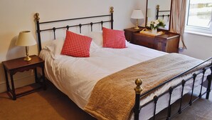 A neatly made bed with a white duvet and two red pillows, a bedside table with a lamp, a wooden nightstand, and a dresser with a mirror. - 3 bedroom accommodation in Winterbourne Steepleton, near Dorchester (Winterbourne Steepleton, near Dorchester)