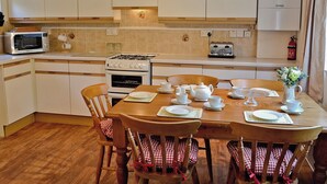 A kitchen with white cabinets, a stove, a microwave, and a dining table set with plates, cups, and a teapot. - 3 bedroom accommodation in Winterbourne Steepleton, near Dorchester (Winterbourne Steepleton, near Dorchester)