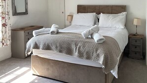 En snyggt bäddad säng med ett mönstrat överkast, två sänglampor och ett träbord vid sängen med en lampa på.