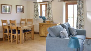 A cozy living room with a dining area, wooden furniture, and large windows with curtains.