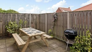 Une table de pique-nique en bois avec des bancs, un barbecue et une clôture en bois, le tout situé dans un jardin.