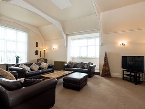 A spacious living room with high ceilings, two leather sofas, a wooden coffee table, and a television on a stand.