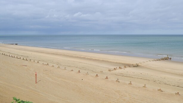 Une vaste plage de sable fin, avec une mer calme et un ciel nuageux.