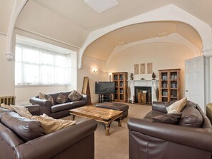 A spacious living room with high ceilings and a fireplace, furnished with leather sofas and a wooden coffee table.