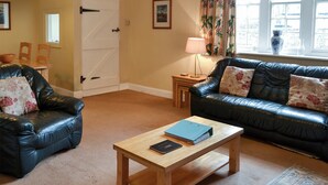 A living room with a wooden coffee table, two leather sofas, a door, and a window with curtains. - Honeysuckle cottage - 23227 (Embleton, near Alnwick)