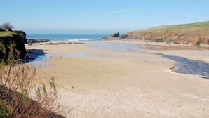 A coastal beach with a clear sky, rocky outcrops, and a grassy hillside. - 2 bedroom accommodation in Padstow (Padstow)