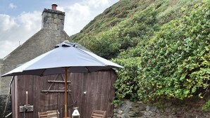 A wooden outdoor seating area with a table and chairs, a lantern, and a large umbrella. - 2 bedroom accommodation in Crovie, Gardenstown (Crovie, Gardenstown)
