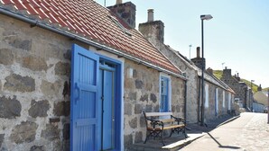 A narrow cobblestone street lined with stone buildings, each with a blue door and a bench outside. - 2 bedroom accommodation in Crovie, Gardenstown (Crovie, Gardenstown)