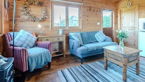 A cozy cabin interior with a wooden ceiling, two windows, a sofa, a chair, a small table, and a lamp. - 1 bedroom accommodation in North Togston near Amble (North Togston near Amble)