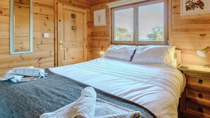 A wooden cabin bedroom with a bed, a nightstand, a dresser, and a window with a view of trees. - 1 bedroom accommodation in North Togston near Amble (North Togston near Amble)