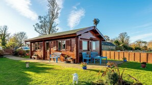 A wooden cabin with a patio area, two blue chairs, and a table. - 1 bedroom accommodation in North Togston near Amble (North Togston near Amble)