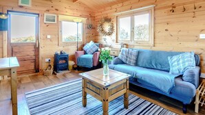 A cozy cabin interior with a wooden floor, a sofa, a table with a vase, and a window with a view of trees. - 1 bedroom accommodation in North Togston near Amble (North Togston near Amble)