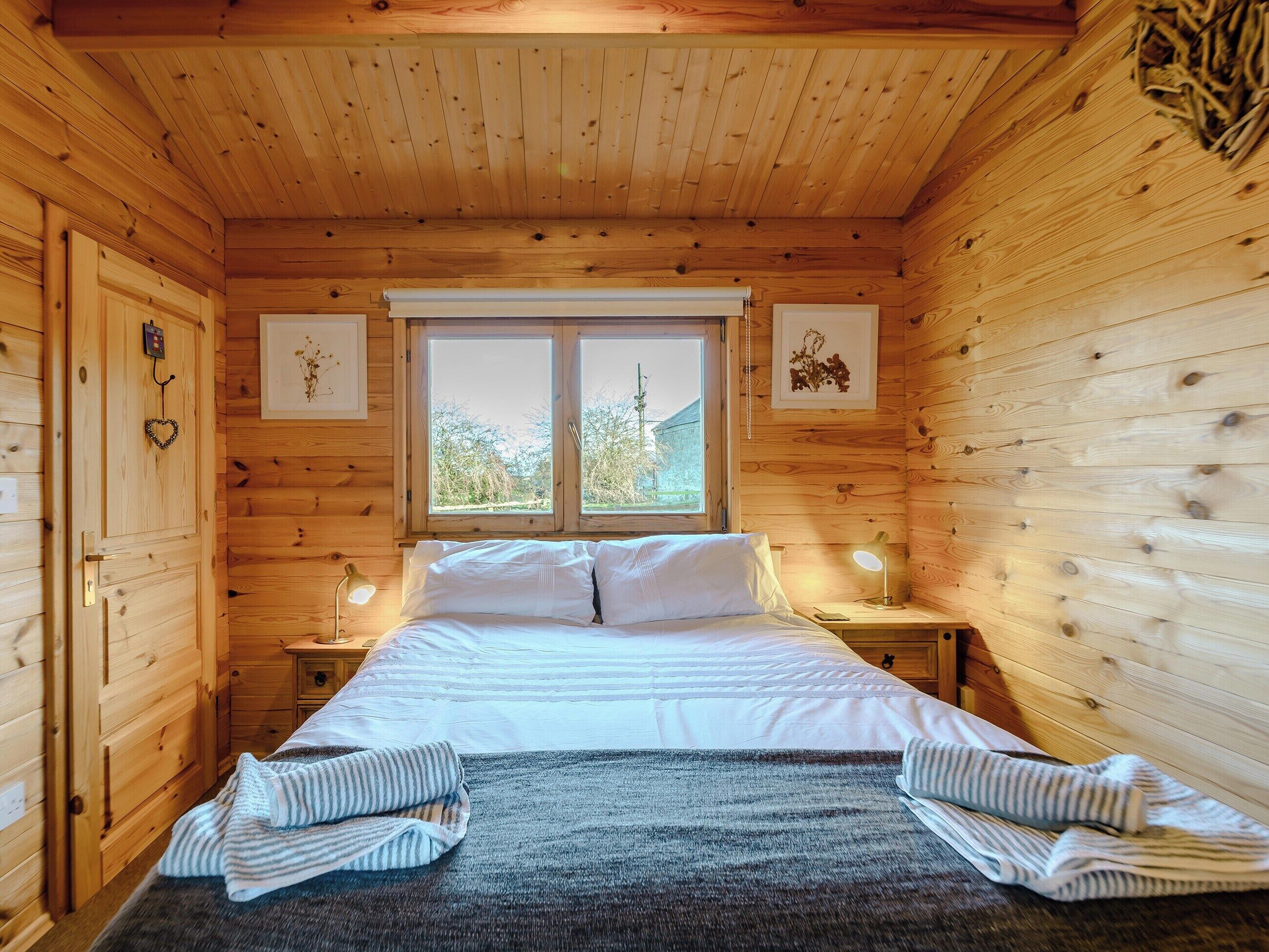 A wooden cabin bedroom with a bed, two bedside tables, a window, and a door.