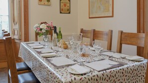 Une table à manger dressée pour six personnes, avec une nappe à motifs, des verres à vin et un vase rempli de fleurs.