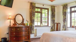 Une chambre à coucher avec un lit, une commode, un miroir, une lampe et un téléviseur fixé au mur.