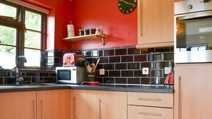Une cuisine avec des meubles de rangement en bois, un mur rouge, un pare-feu en carreaux noirs et une horloge.