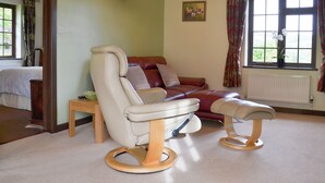 Un salon avec un canapé en cuir, deux fauteuils inclinables, une petite table et une fenêtre avec des rideaux.