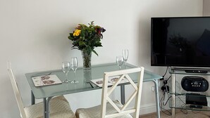 A dining area with a glass table, two chairs, a vase with flowers, and a television. - 1 bedroom accommodation in Little Tathwell, near Louth (Little Tathwell, near Louth)
