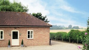 A brick building with a tiled roof, a gravel driveway, and a hedge with pink flowers. - 1 bedroom accommodation in Little Tathwell, near Louth (Little Tathwell, near Louth)