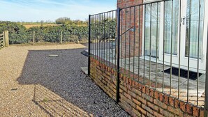 A brick building with a metal gate and a gravel driveway leading to a glass door. - 1 bedroom accommodation in Little Tathwell, near Louth (Little Tathwell, near Louth)