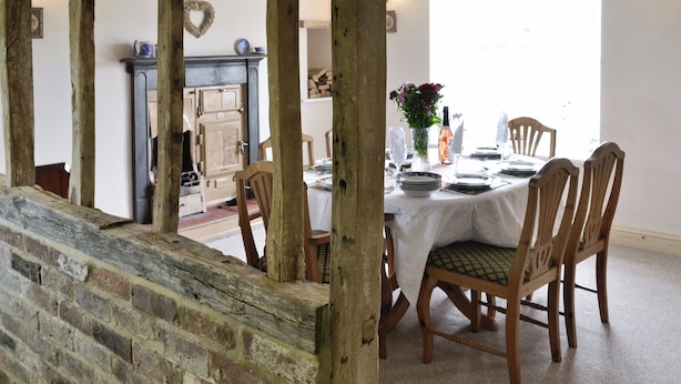 A dining area with a table set for four, wooden chairs, a fireplace, and a brick wall. - SHRUBBERIES COTTAGE - DC5472 (Old Liverton Village, near Staithes)