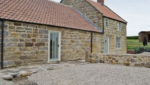 A stone building with a red-tiled roof, a gravel driveway, and a wooden fence. - SHRUBBERIES COTTAGE - DC5472 (Old Liverton Village, near Staithes)
