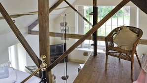 A loft-style room with exposed wooden beams, a wicker chair, a black sofa, and a hanging light fixture. - SHRUBBERIES COTTAGE - DC5472 (Old Liverton Village, near Staithes)