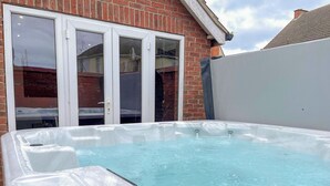 Ein Whirlpool in einem Garten mit einem Ziegelhaus und einer weißen Mauer.