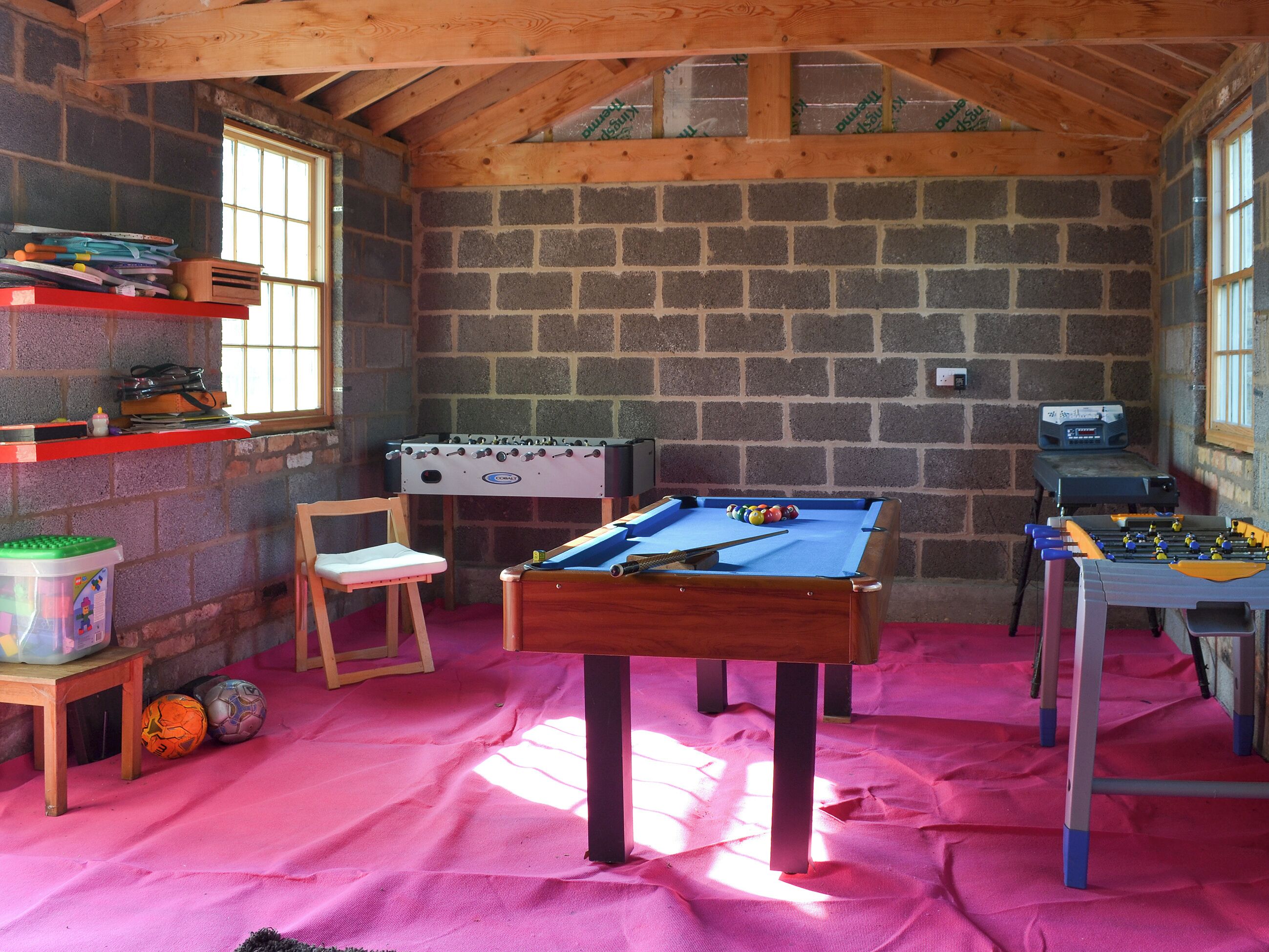 Una habitación con mesa de billar, mesa de futbolín y pared de ladrillo.