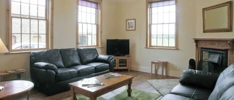 A living room with a black leather sofa, a wooden coffee table, and a television on a stand.
