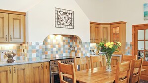 Una cocina con armarios de madera, salpicadero de azulejos, estufa y una mesa de comedor con sillas.